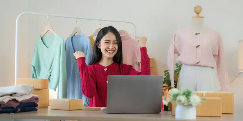 A shop owner celebrating in front of a laptop surrounded by stock